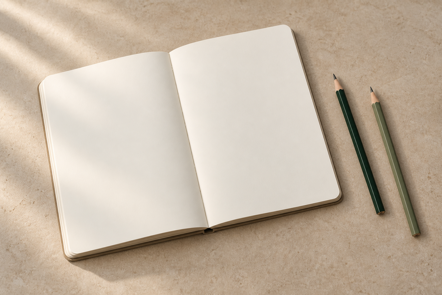 Cuaderno abierto en blanco y dos lápices sobre piedra, con luz rasante
